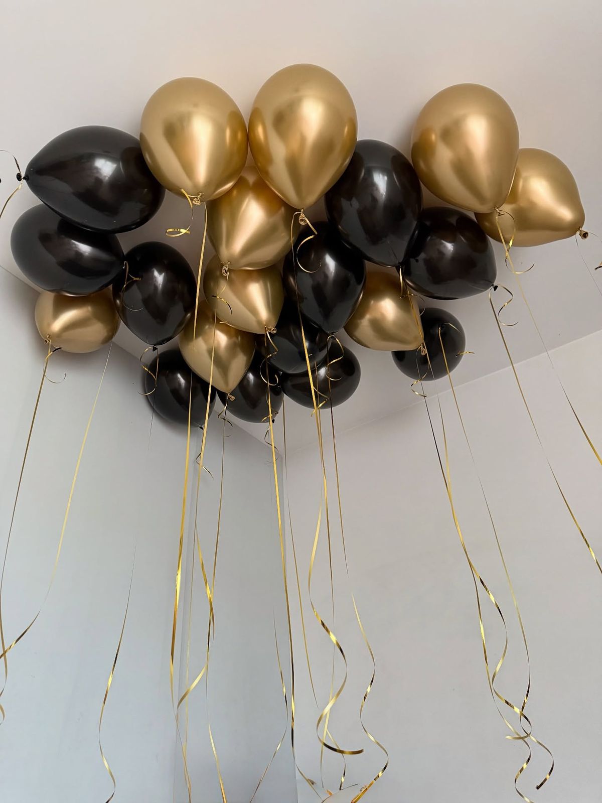 Decorative arrangement of black and gold balloons with ribbons on a light background