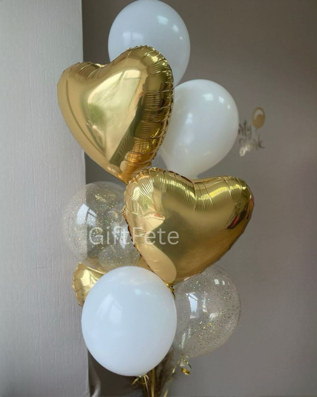 Gold heart-shaped balloons with white and clear balloons on a neutral background