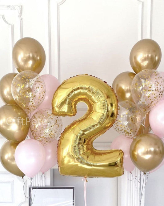 Gold number 2 balloon surrounded by pink and gold balloons against a white wall.