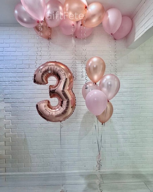 Rose gold and pink balloons with a number 3 balloon against a tiled wall.