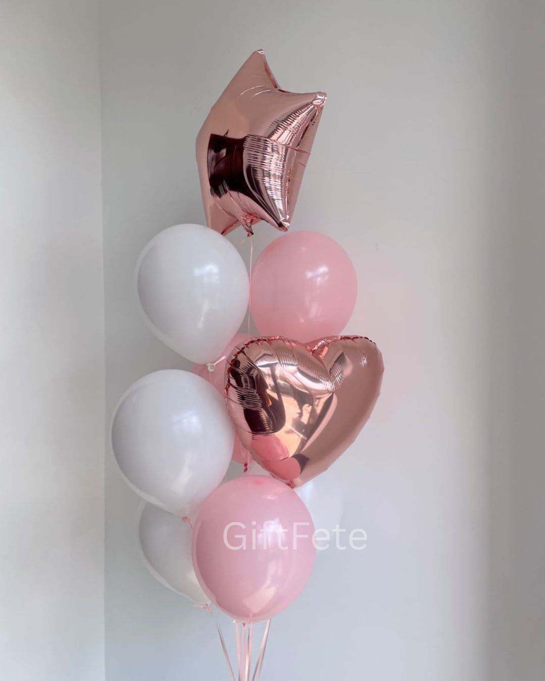 Balloon bouquet with pink, white, and rose gold balloons on a plain background